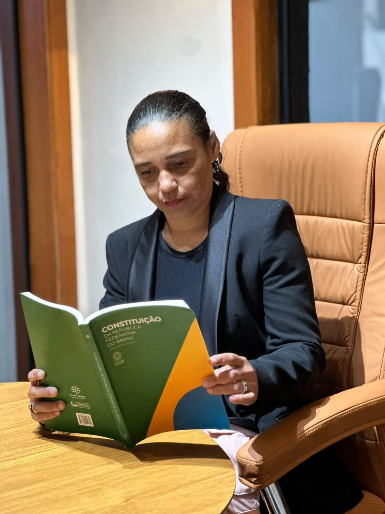 Jack Lopes, candidata a deputada federal, sentada no Comitê Central de campanha lendo a Constituição Federal do Brasil, capítulo sobre meio ambiente, concentrada em estudo com o livro aberto sobre a mesa